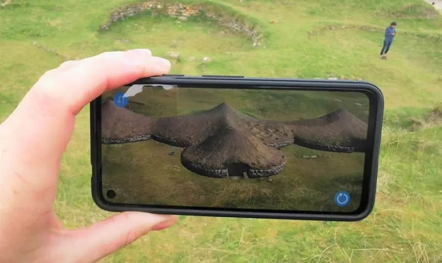 A visitor to Cladh Hallan on Uist uses augmented reality through the camera of their phone to see what the original structures on the site looked like.