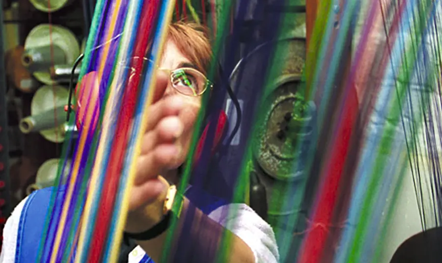 A person wearing ear protection stands behind brightly coloured threads.