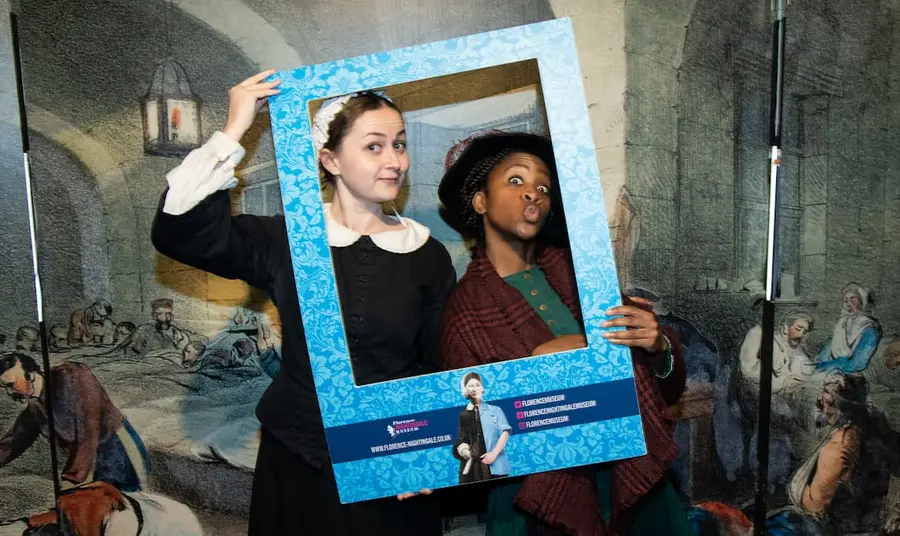 Two people in historic nursing outfits depicting Mary Seacole and Florence Nightingale, holding a frame to their faces