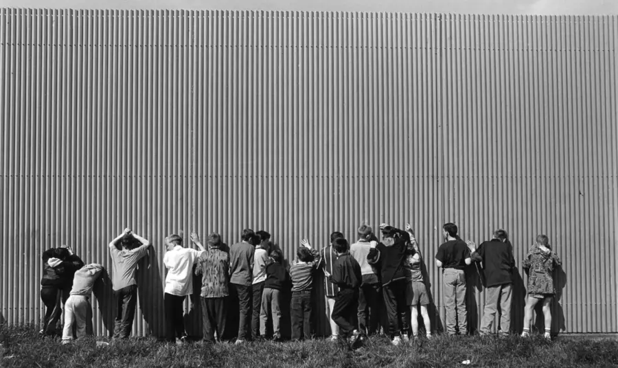 A group of young boys sneak a view through gaps in a Belfast peace wall.