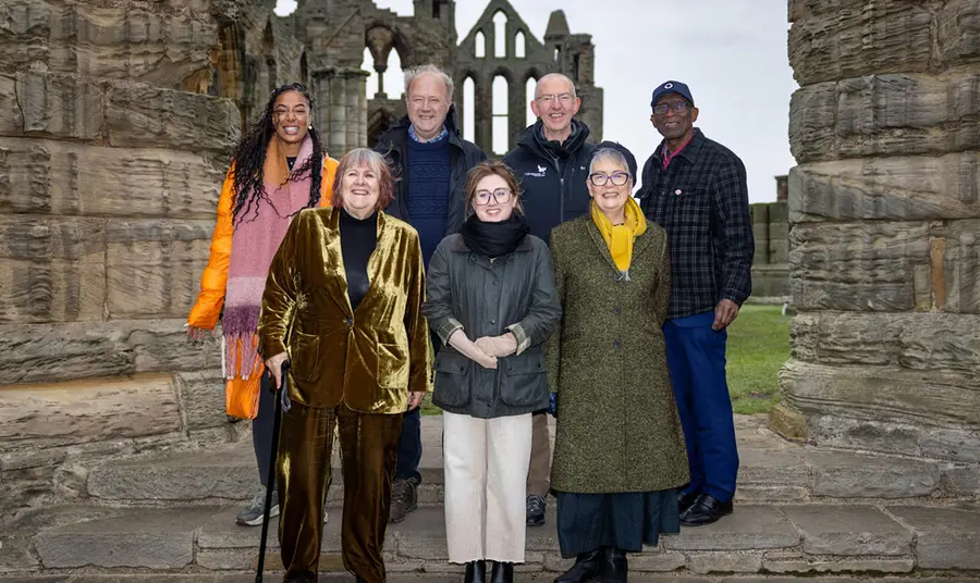 A group of seven men and women standing in front of the ruins of Whitby Abbey