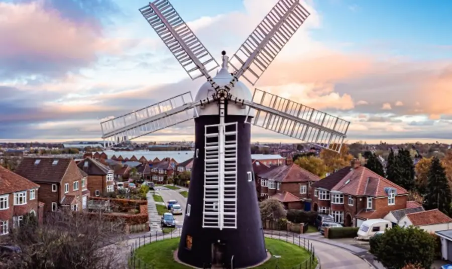 A windmill with houses in the background set against a blue sky