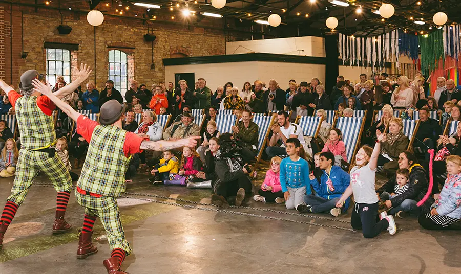 Two clowns performing in front of a crowd seated in deck chairs. Photograph by Graeme Oxby.