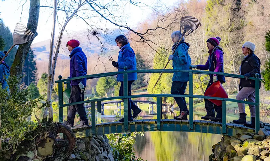 People walking across a bridge with gardening equipment in their hands