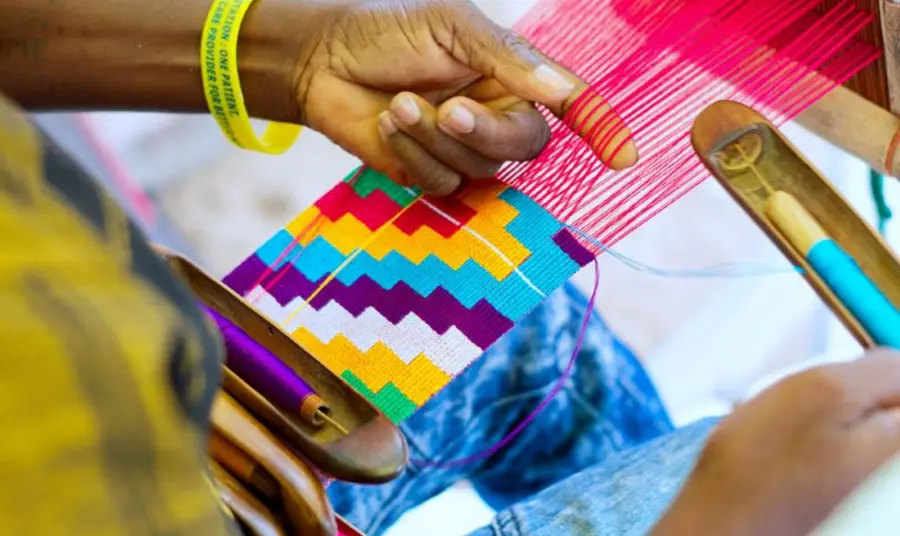 A close-up of a person's hands weaving colourful threads on a loom