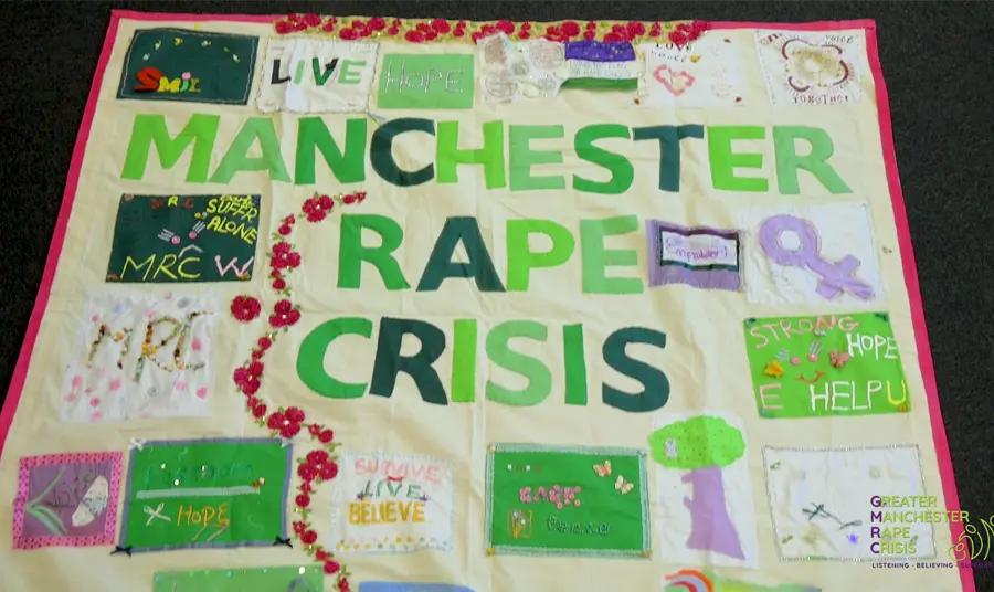 The banner has the words Manchester Rape Crisis in the middle with other phrases and images stitched around it