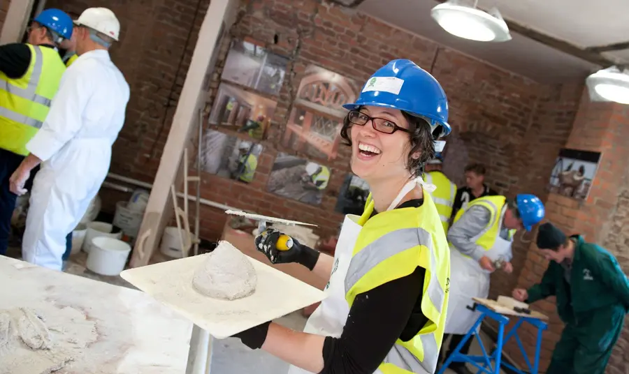 A smiling woman holding a board with plaster on it and a trowel