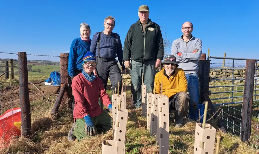 A group of volunteers pose behind some newly planted saplings, which are protected with tubing.