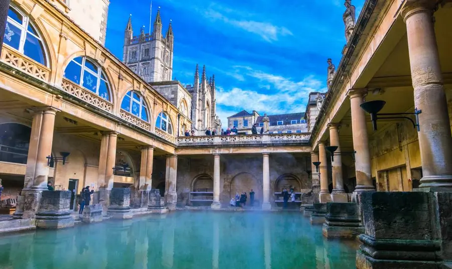 Looking across the water at the Roman Baths in Bath, people standing on the edges and looking down from a walkway above with