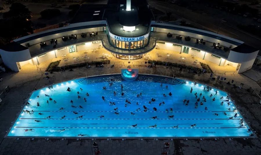 An aerial view of people swimming in the Lido lit up at night