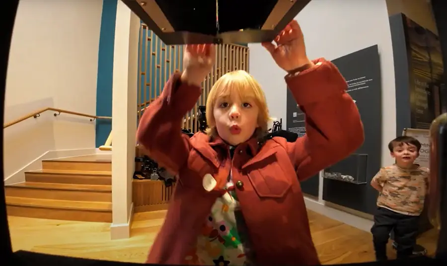 A young boy opening a box at a museum with a 'wow' expression on his face