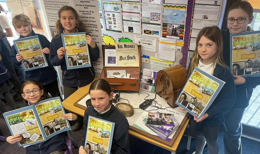 A group of school children hold books about life during the second world war and pose around a display related to the second world war