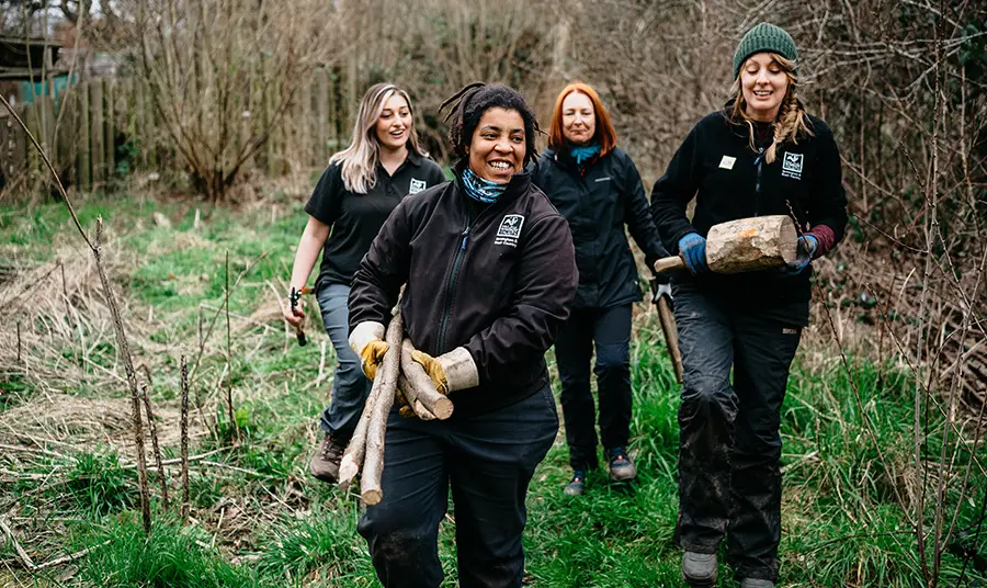 Three women carrying logs in a park