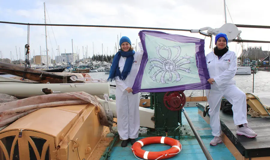Photograph of two women holding up a flag while standing on a boat.