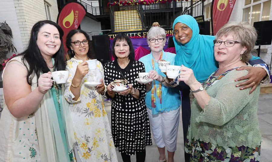 A group of six women standing side by side with raised tea cups in their hands