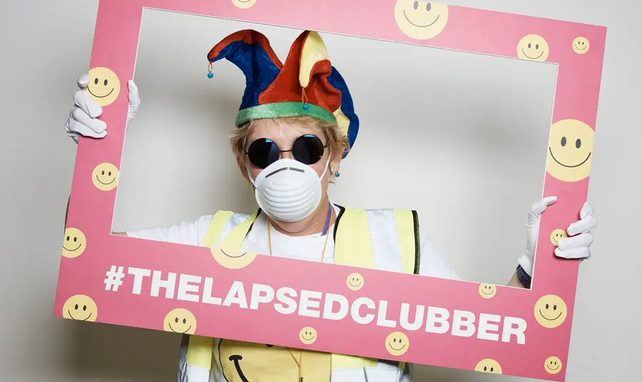 A lapsed clubber holding a picture frame, dressed in typical clubbing paraphernalia from the late 80s