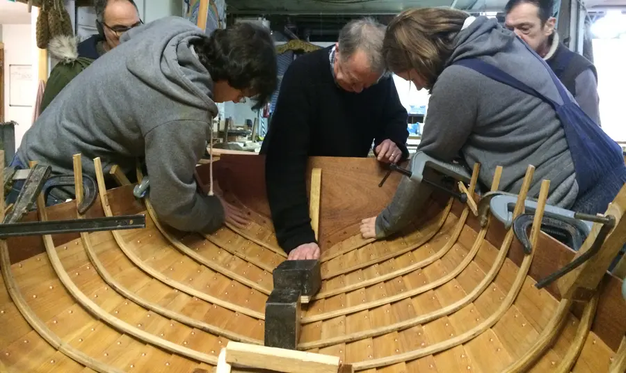 People working on the inner side of the hull of a wooden boat