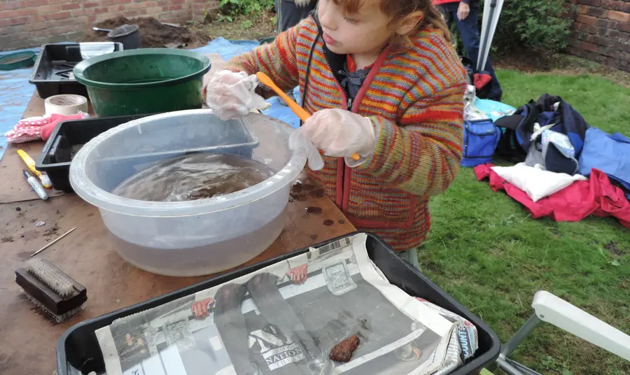 A child using a toothbrush to wash a sherd of pottery in a basin of water