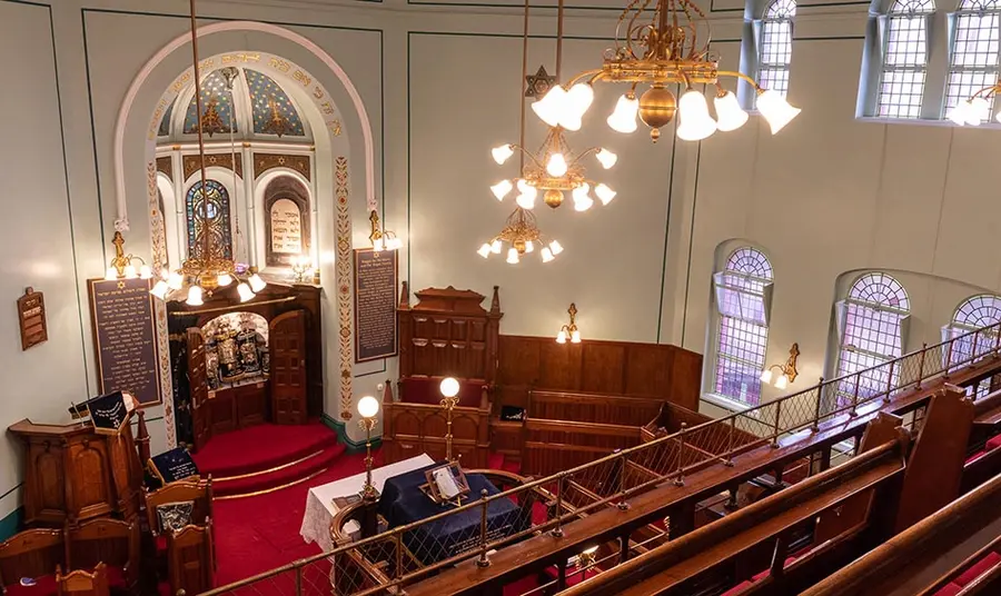 Interior of Leicester synagogue: a large room with a cabinet containing the torah scrolls, lecterns and seating in carved wooden pews