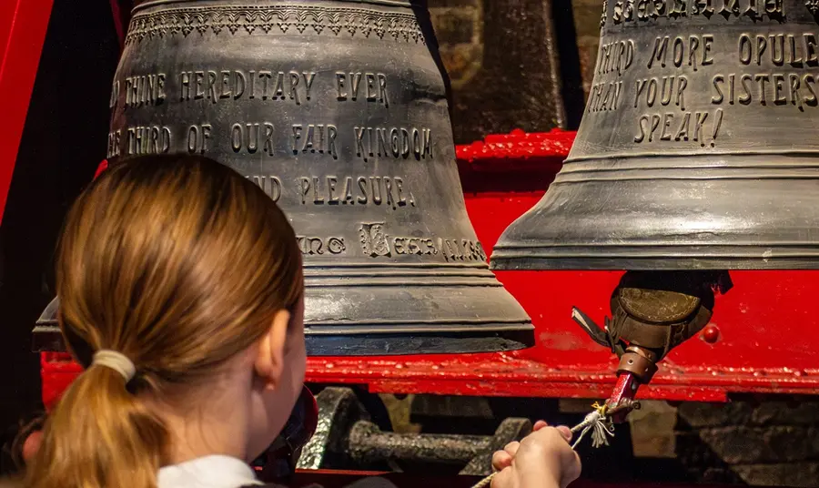 A visiting schoolgirl rings a cast iron bell on a bracket.