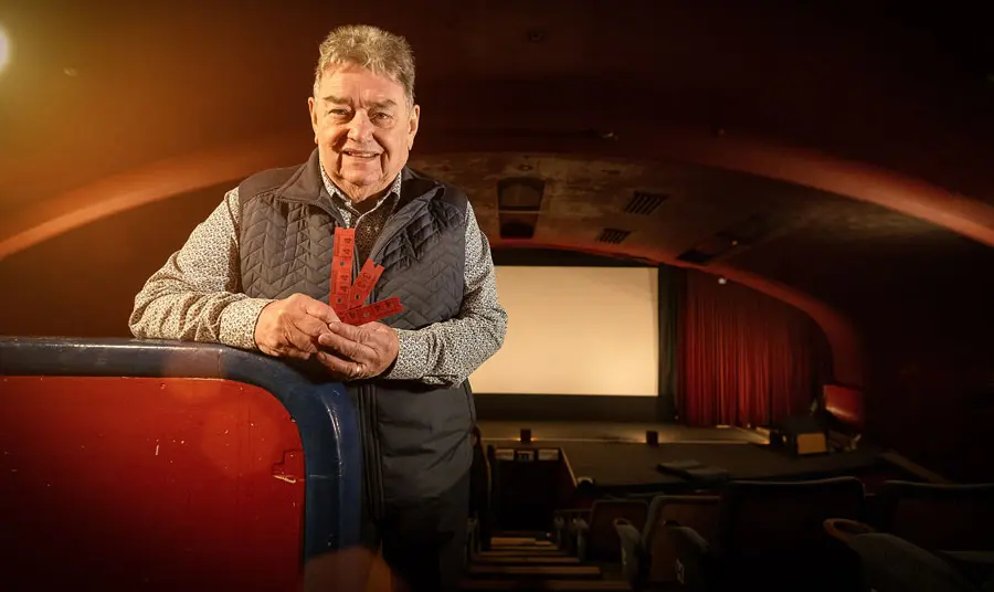 A man stands inside the arched cinema holding ticket stubs