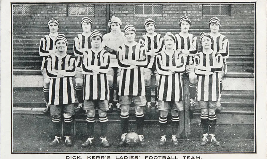 A black and white postcard of a woman’s football team arranged in two rows, wearing striped uniforms.