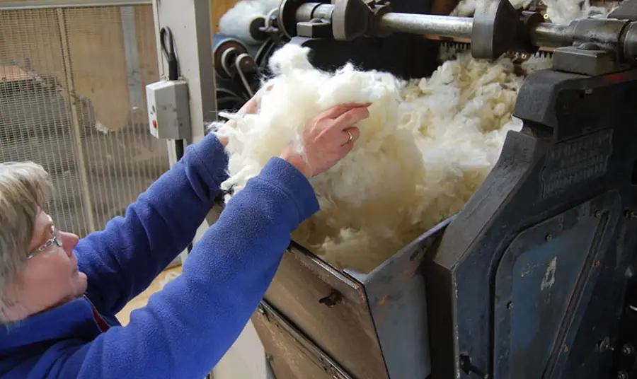 A person feeding wool into a piece of machinery 