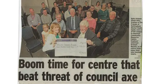 A newspaper clipping: the headline reads 'Boom time for centre that beat threat of council axe' and the photo shows a group of people sitting holding a cheque