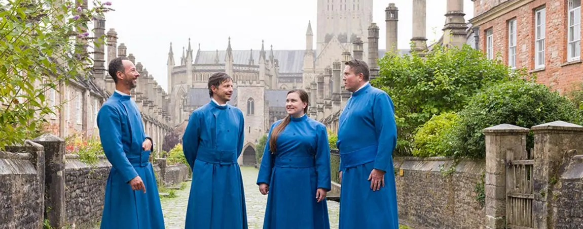 Members of Wells Cathedral’s Vicars’ Choral wear long blue robes and stand outside their medieval stone and brick homes on Vicars’ Close in Wells