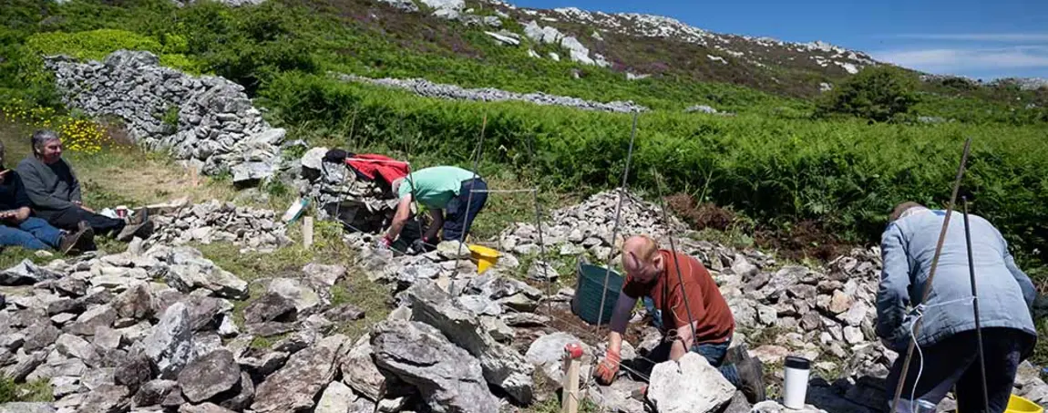 People building dry stone walls on a hillside on a sunny day