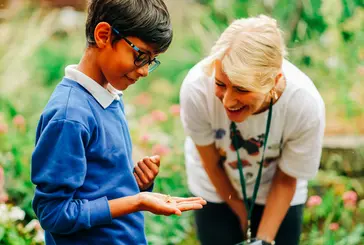 A child holds a butterfly while a guide smiles at him