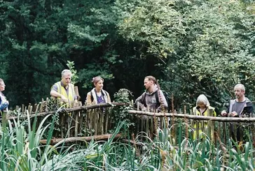 People stand on a wooden bridge surrounded by plants and greenery