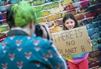 A child having their photograph taken, holding up a cardboard sign that reads: There is no planet B