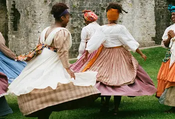 A group of women in period dress dancing outside Porchester Castle.