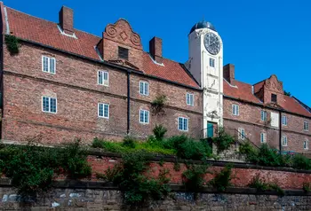 A large red brick building with a white tower featuring a clock at the centre of its length.