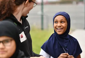 An adult talks to a child wearing a head scarf.