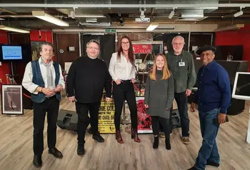 Six people posing for a picture in front of a Jazz music archive, including posters and frames 