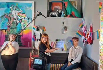 Three young people making a film, one person is holding a microphone, another a clapperboard, and one person is waiting to be interviewed