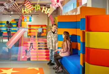 Young children are sat on colourful seating inside the museum, while others are stood on the stairs in the background