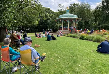 People sitting in a sunny park, near a bandstand