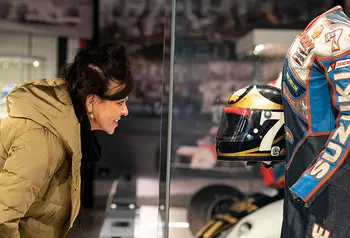 Woman looking into a glass case displaying Barry Sheene's racing leathers and helmet