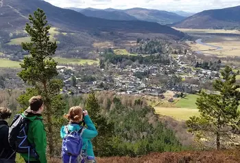 Three people look down over a valley with mountains in the distance