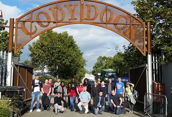 Crowd of people under a rust-coloured metal arch, which reads Cody Dock.