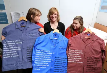 Three participants hold up exhibits including shirts with text written on them