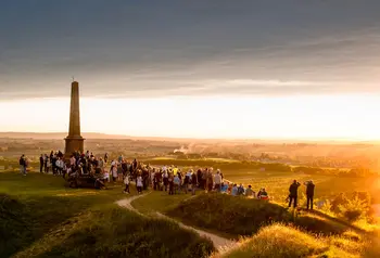 A large group of people stand on top of Ham Hill summit at sunset