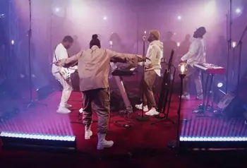 A band on stage singing, playing the keyboard and guitar.