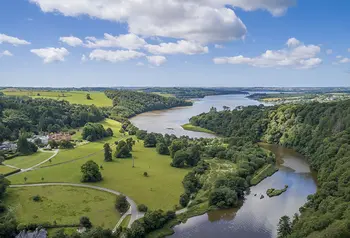 Aerial view over green valley with trees, grass, curving river and blue sky