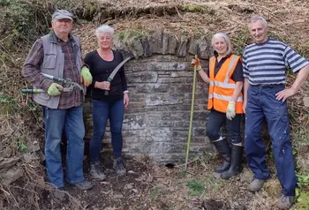 Four people stand in a woodland holding gardening tools