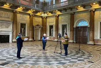 Three people recording film in large stately room