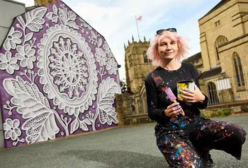 An artist kneels in front of a painted wall with an intricate pattern on a purple background